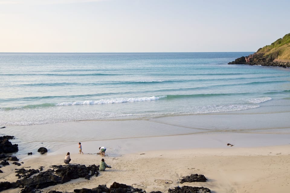 A beach with calm waves, rocky shoreline, and a wooden walkway along the cliff.