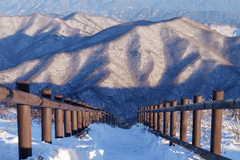A snow-covered mountain range with a wooden fence in the foreground.