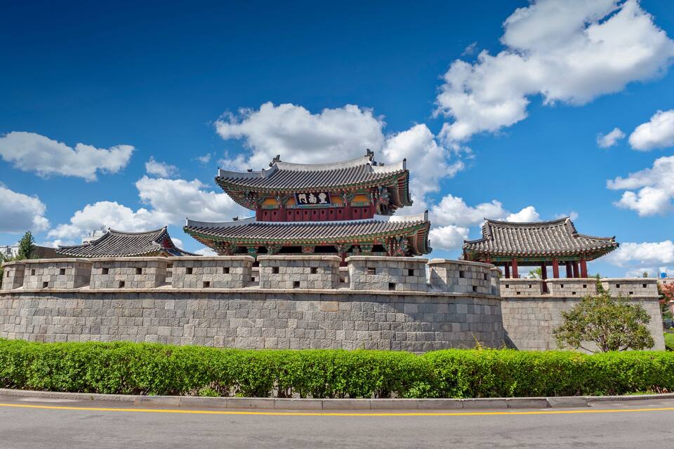 A traditional multi-tiered pagoda with ornate roofs, a stone wall, and a clear blue sky with clouds.