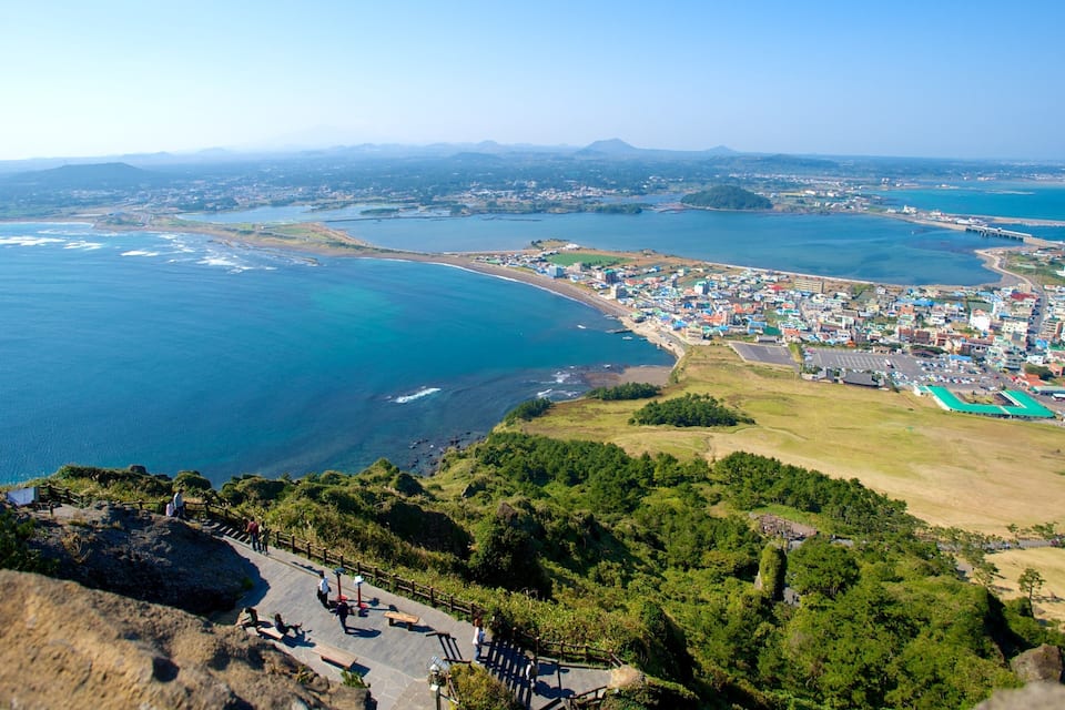 An aerial view of a coastal town with a beach, a marina, and a mountainous backdrop.