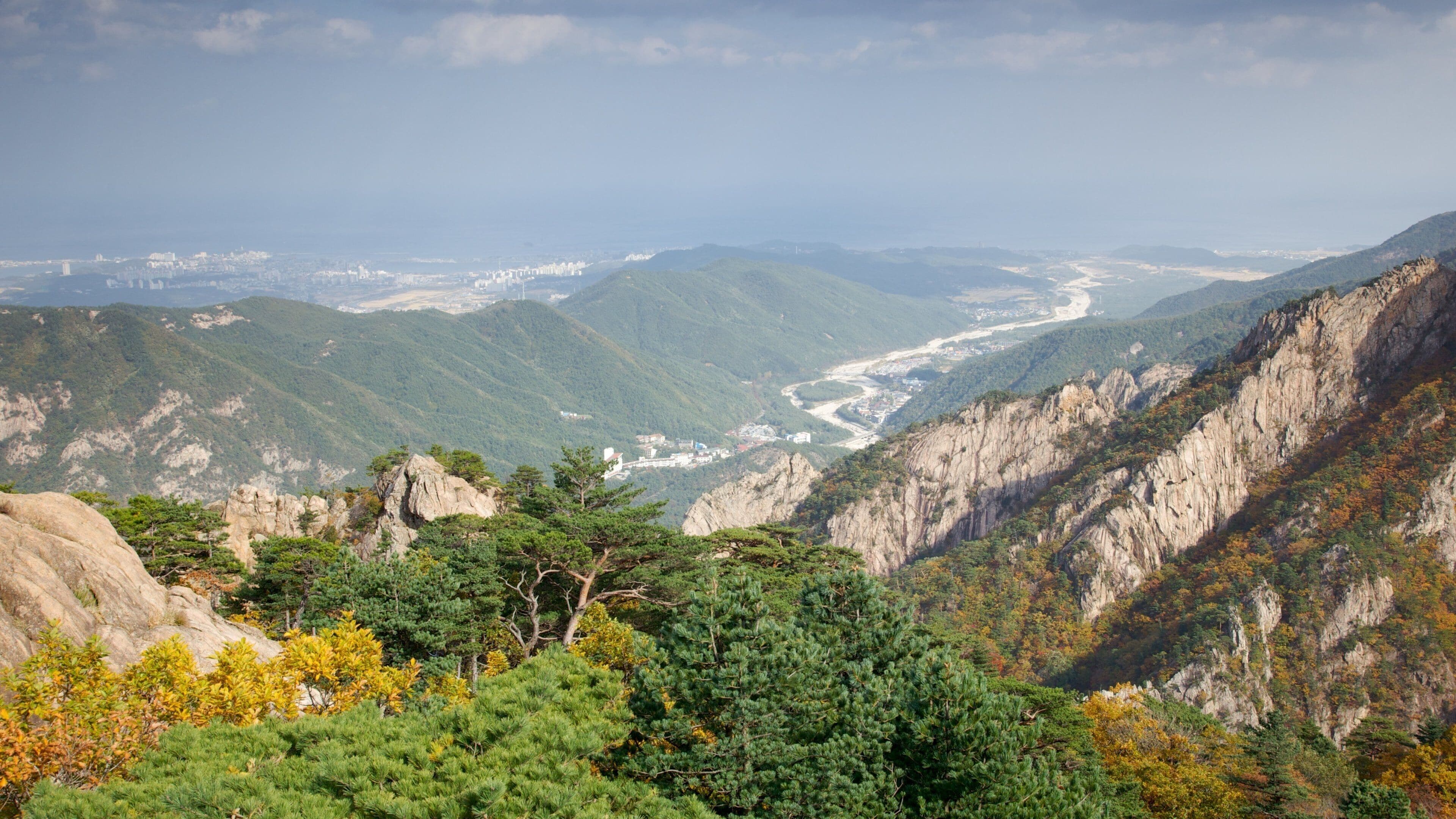 A mountainous landscape with a river valley, dense forests, and rocky cliffs.