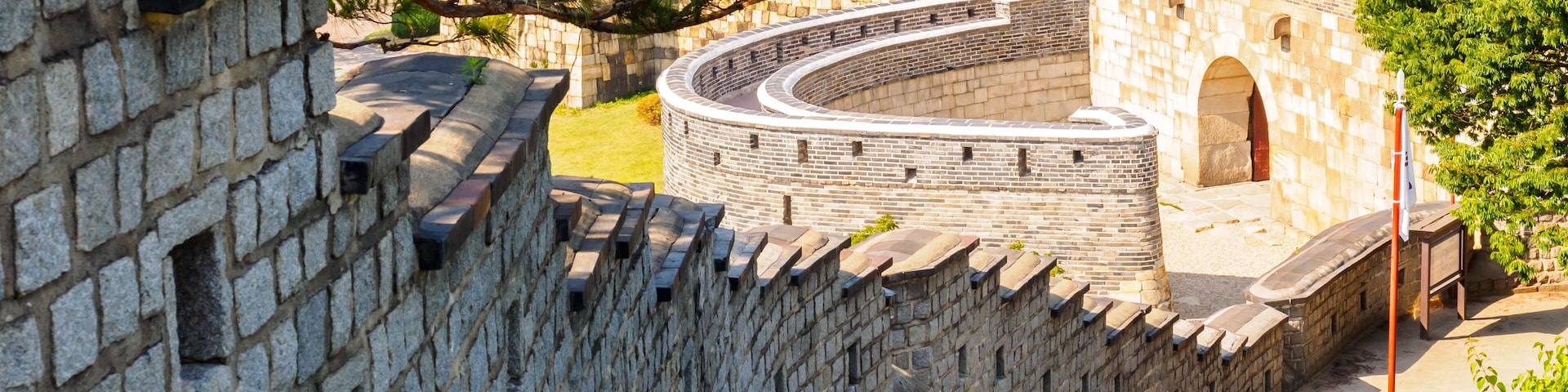 Um muro de pedra com um caminho sinuoso que leva a edifícios tradicionais.
