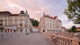 Eine Kopfsteinpflasterstraße gesäumt von historischen Gebäuden, eine Brücke mit aufwendigen Brüstungen und ein Schloss in der Ferne auf einem Hügel.