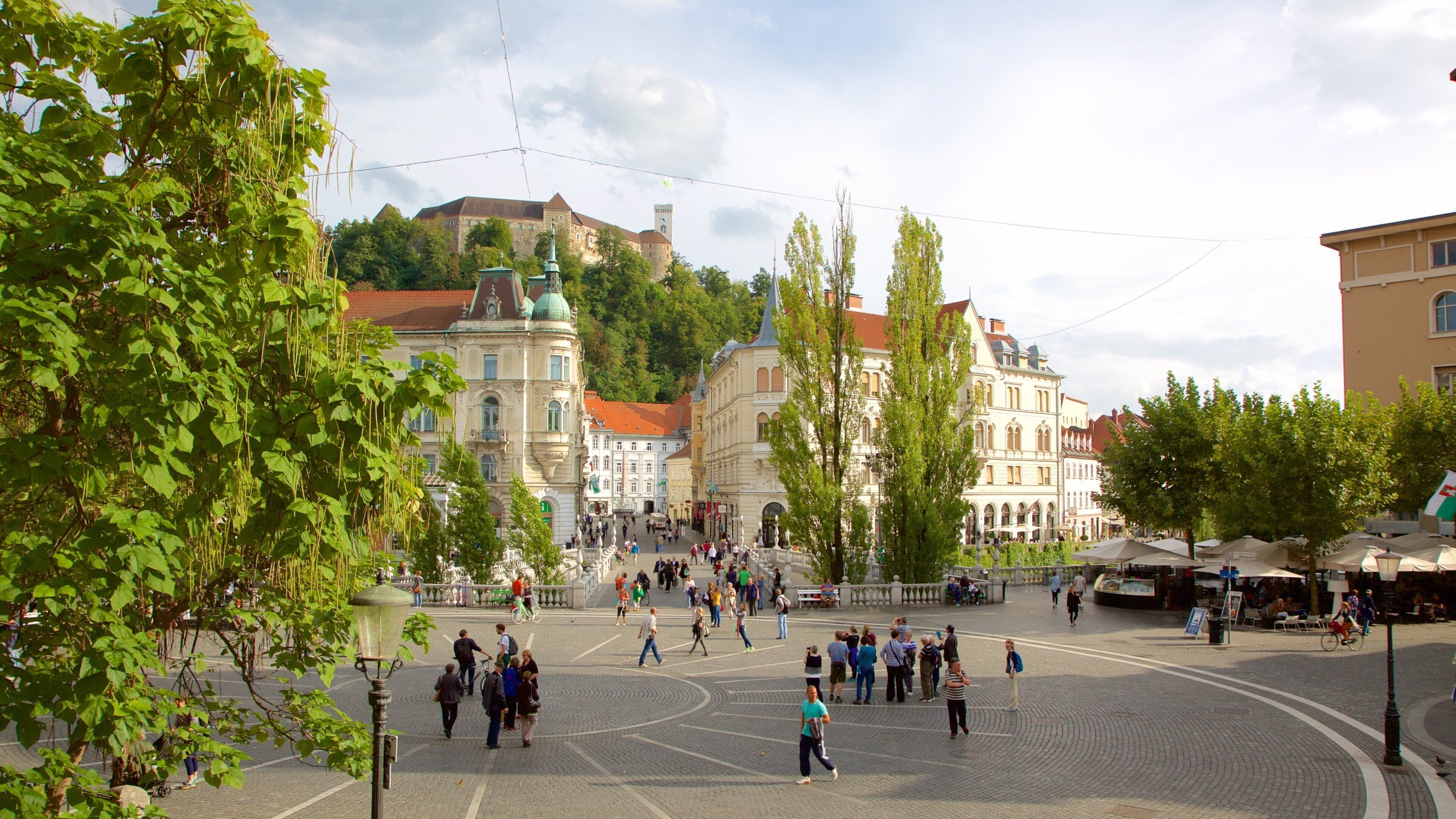A bustling square with historic buildings, a prominent tower, and a statue in the center.