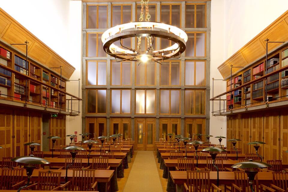 Uma biblioteca com estantes de madeira, mesas, cadeiras e um grande candelabro.