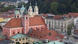 A historic town with red-tiled roofs, a prominent church with a clock tower, and surrounding buildings with varied architectural styles.