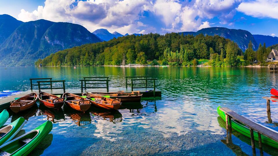 A serene lake with boats docked at a pier, surrounded by lush green mountains and a church.
