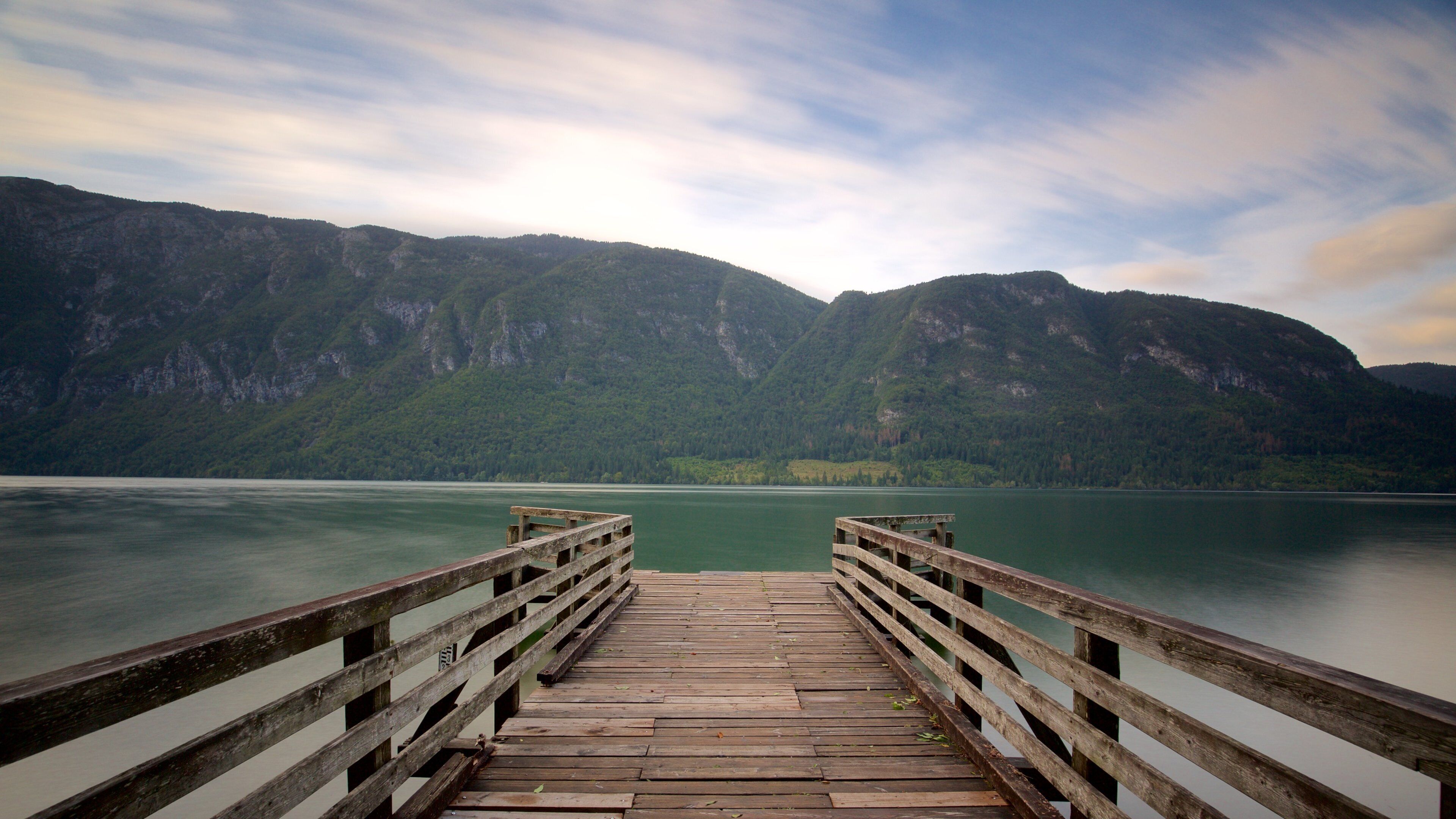 A wooden pier leading to a calm lake surrounded by mountains.