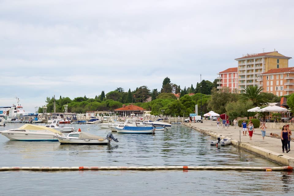 Ein Yachthafen mit vor Anker liegenden Booten, eine Uferpromenade und Gebäude im Hintergrund.