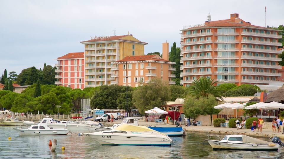 A marina with several boats, including a blue and a white one, and a hotel named Hotel Riviera in the background.