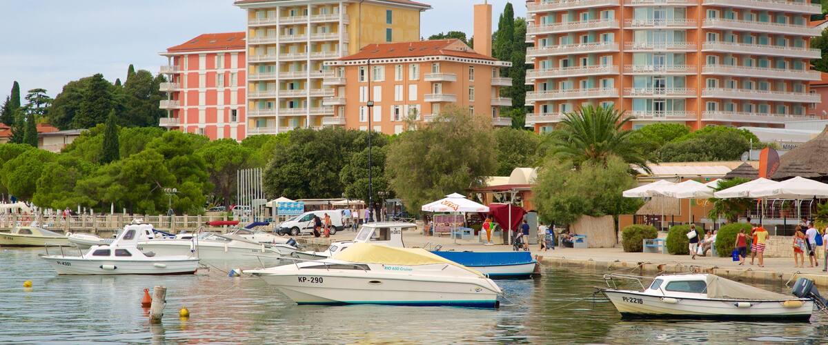 A marina with several boats, including a blue and a white one, and a hotel named Hotel Riviera in the background.