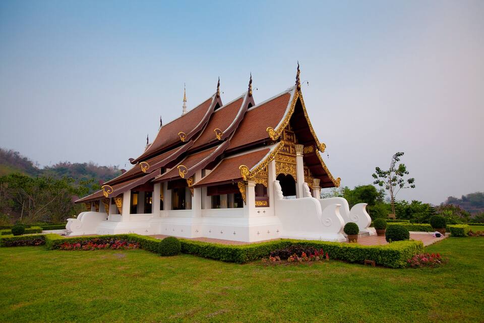 A traditional Thai temple with ornate golden decorations and a white facade, surrounded by well-maintained gardens.