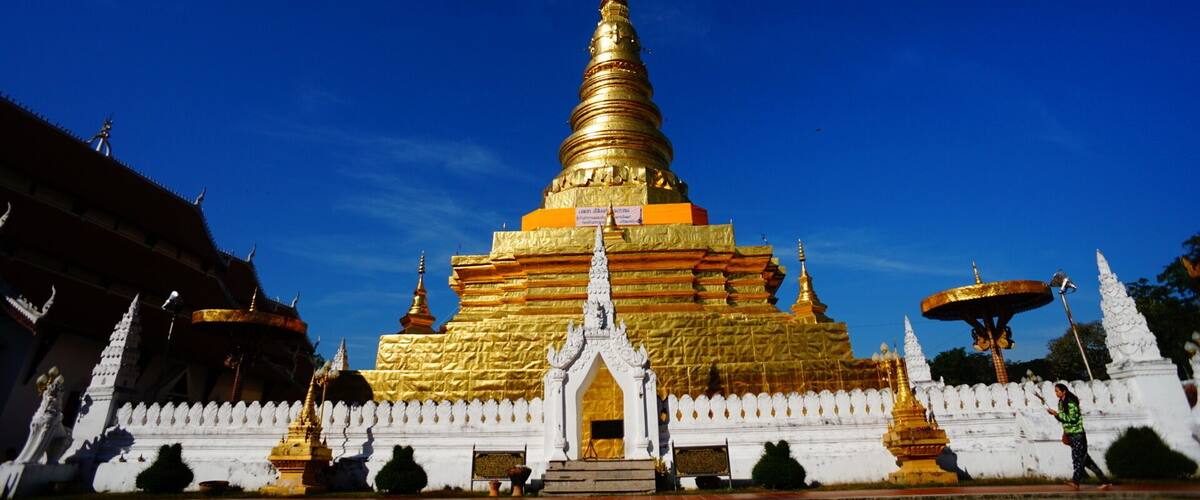A multi-tiered golden stupa with a white entrance, surrounded by white walls and smaller golden structures.