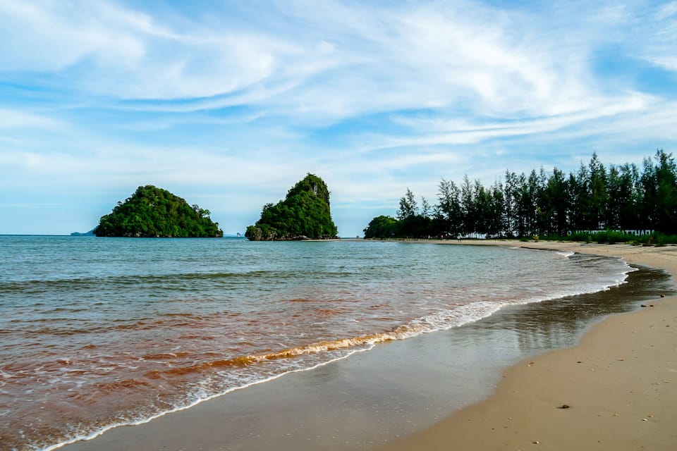 A beach with two green islands in the distance, a sandy shore, and a clear sky.