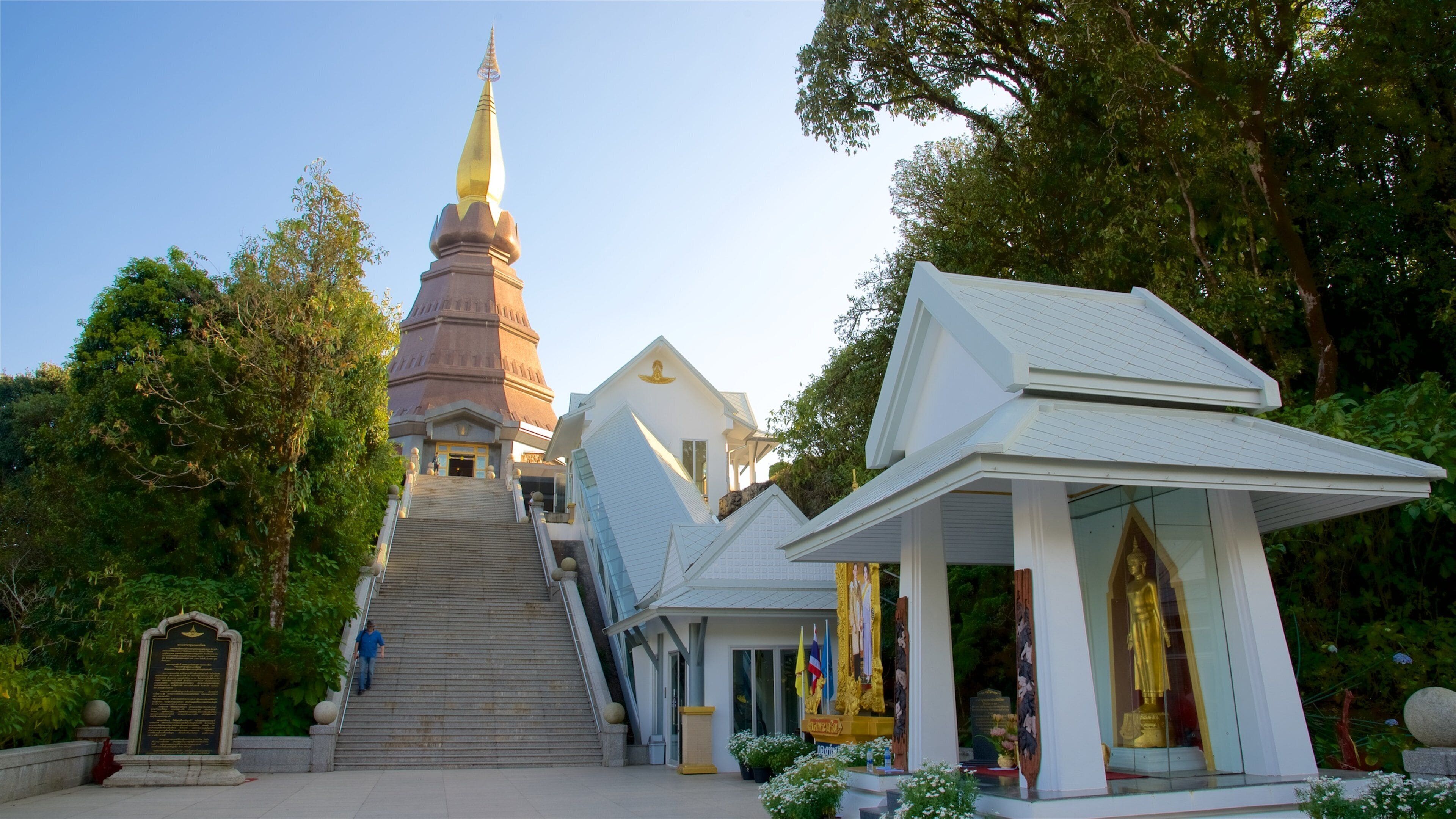 A temple complex with a prominent golden spire, a staircase leading up to the entrance, and a white pavilion with a golden statue.