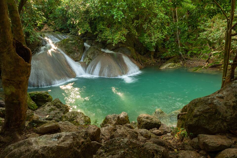 Uma cascata deságua em uma piscina azul-turquesa, cercada por pedras e vegetação verde densa.