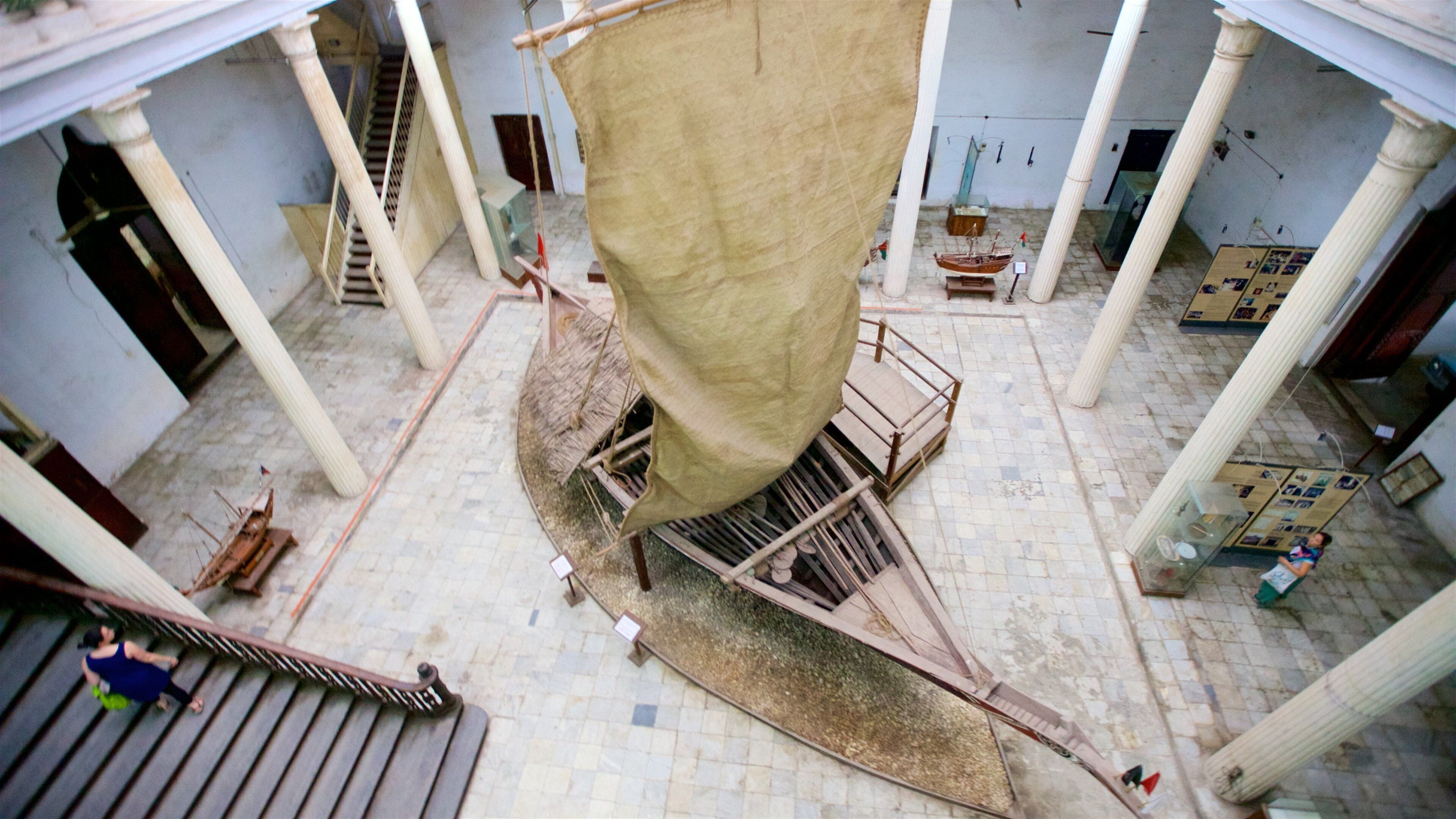 A large sail hanging from a wooden structure in an indoor setting with tiled floors and columns.