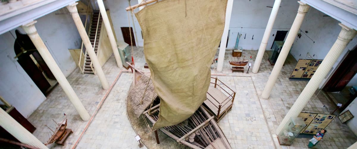 A large sail hanging from a wooden structure in an indoor setting with tiled floors and columns.