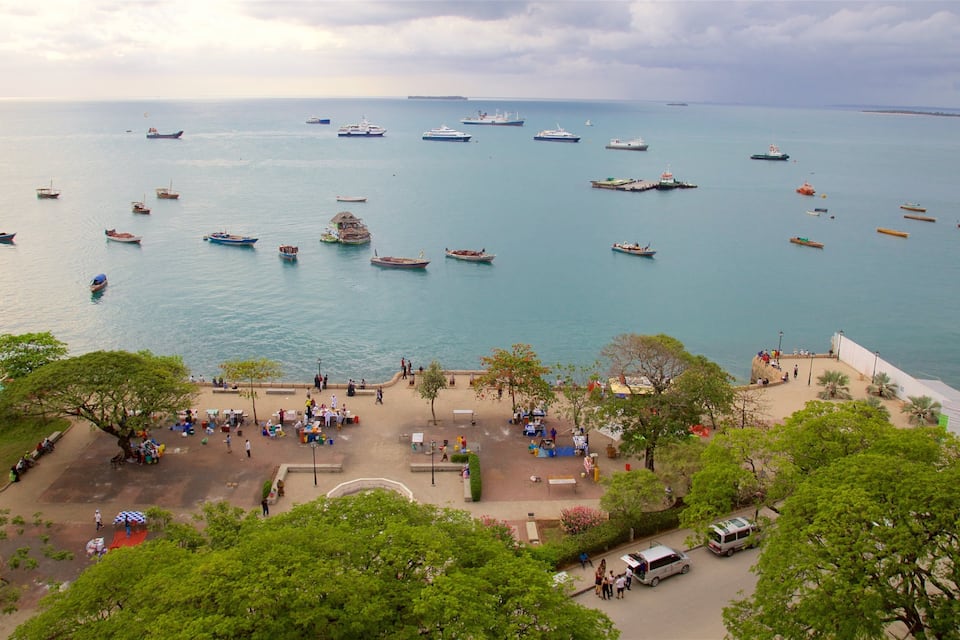 Une ville côtière dotée d’un port de plaisance où sont amarrés différents types de bateaux, d’une promenade animée et d’une végétation luxuriante.