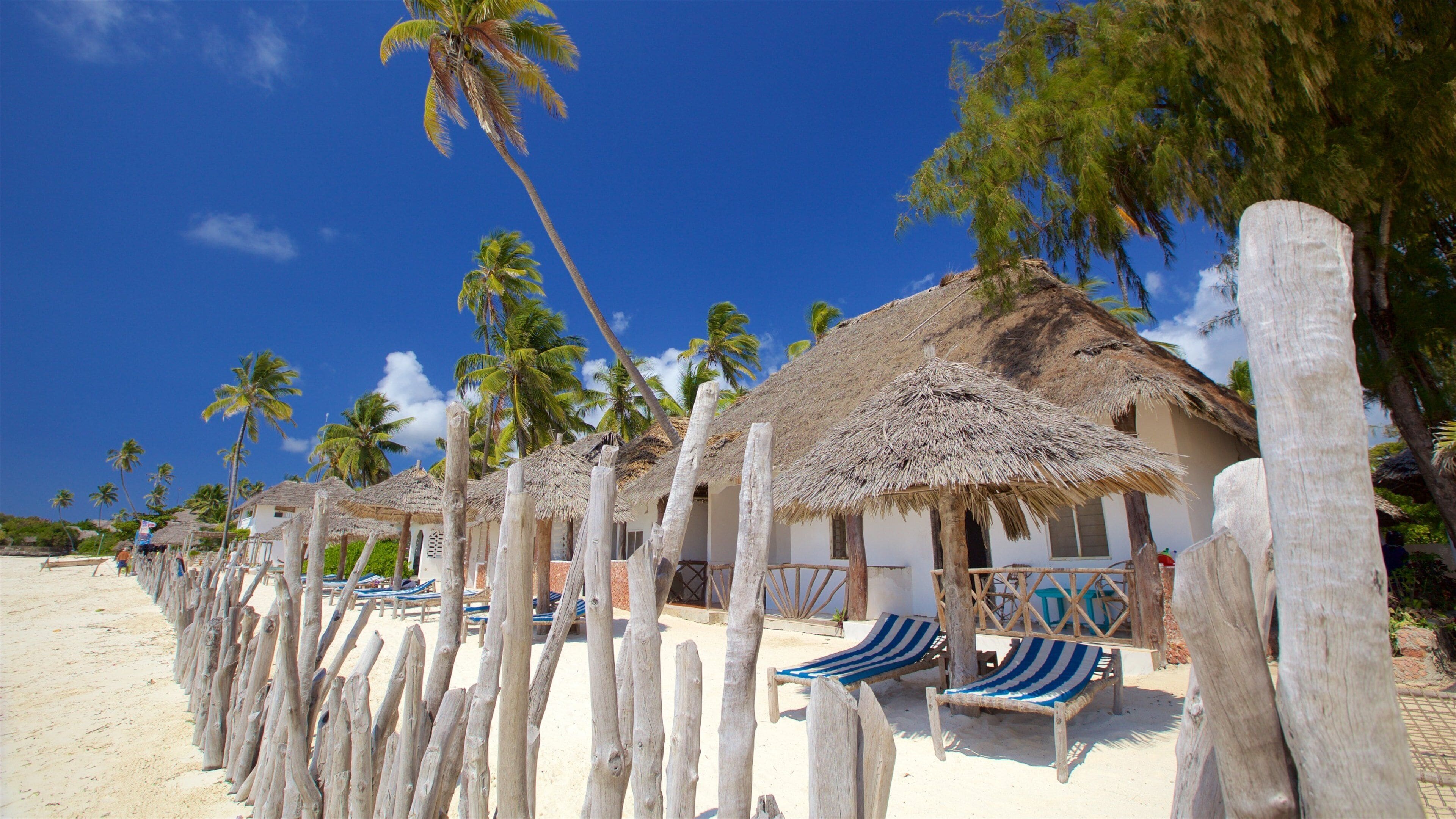 A beach with thatched-roof huts, palm trees, and striped beach chairs.