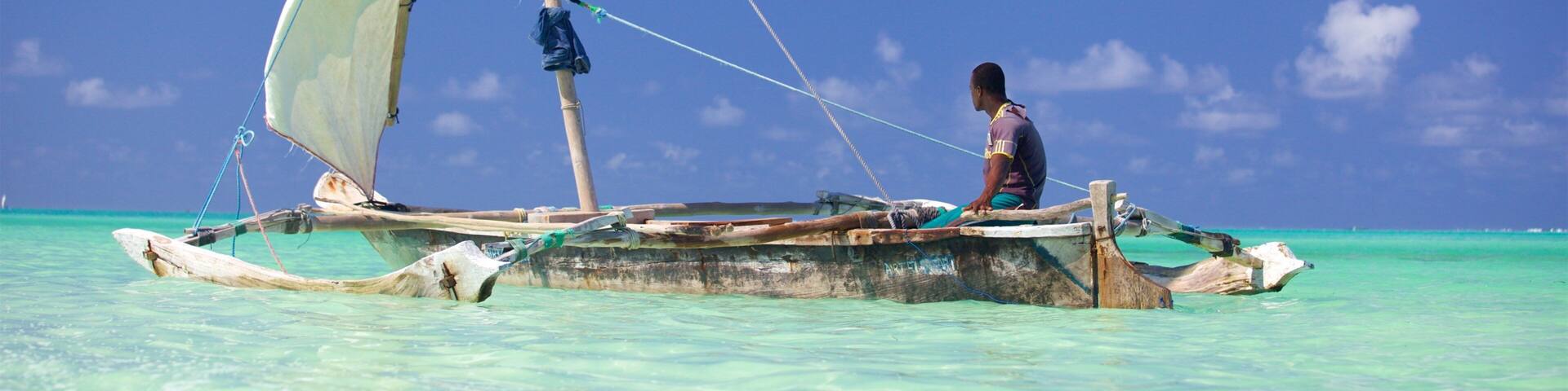 A traditional sailboat with a person on board, floating on turquoise waters under a clear blue sky.