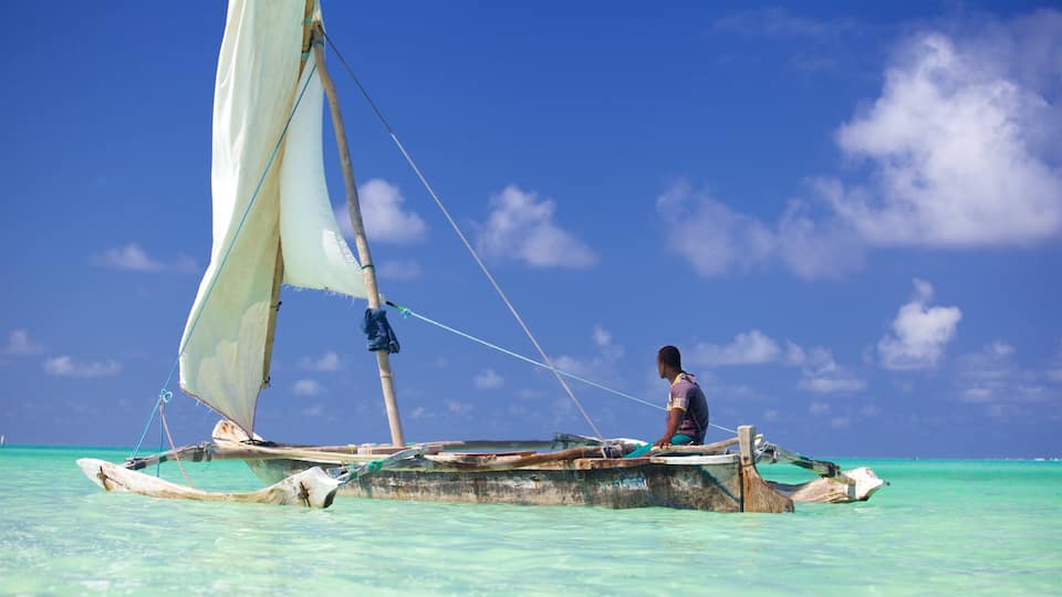 A traditional sailboat with a person on board, floating on turquoise waters under a clear blue sky.