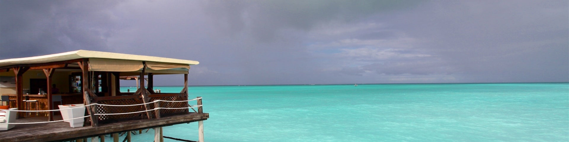 A wooden overwater structure with a covered seating area overlooking turquoise waters.
