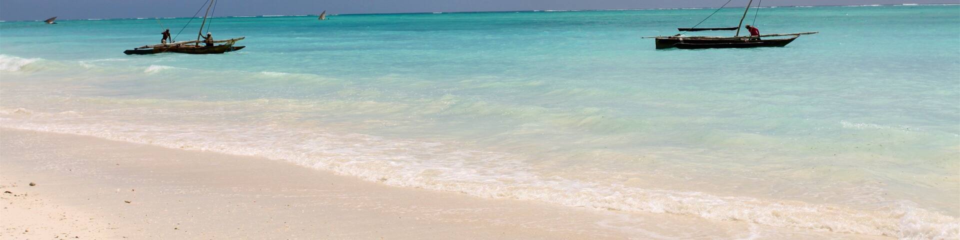 Una playa con agua turquesa cristalina y dos barcos anclados cerca de la orilla.