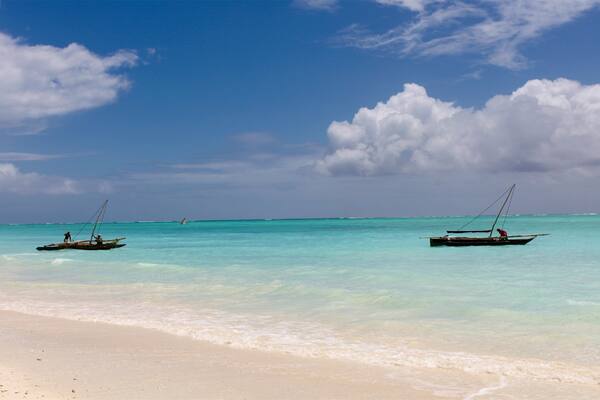 Une plage bordée d’une eau turquoise et limpide, avec deux bateaux ancrés près du rivage.