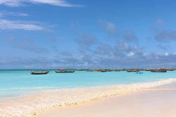 Une plage aux eaux turquoise et limpides, avec plusieurs bateaux ancrés au loin.