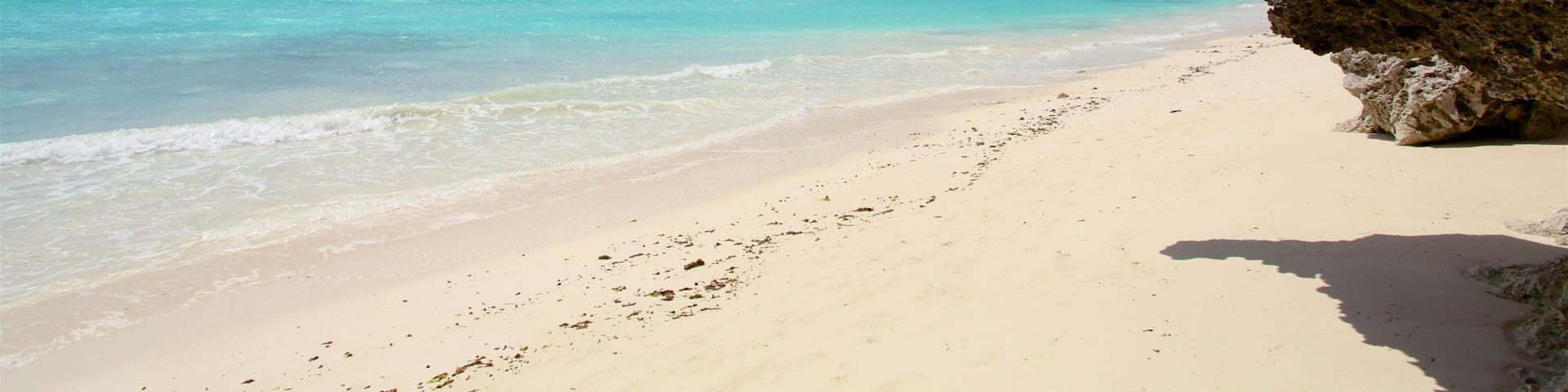 A beach with clear turquoise water, white sand, and a rocky cliff.
