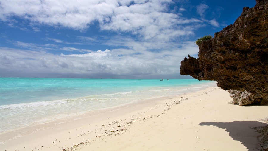Une plage à l’eau turquoise et limpide, au sable blanc, bordée d’une falaise rocheuse.