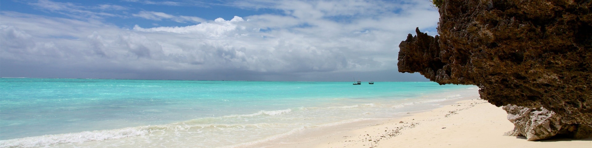 Una playa con agua turquesa cristalina, arena blanca y un acantilado rocoso.