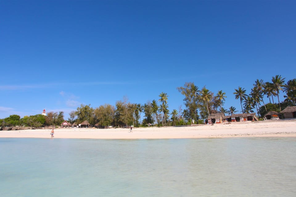 A beach with clear turquoise water, palm trees, and thatched-roof huts.