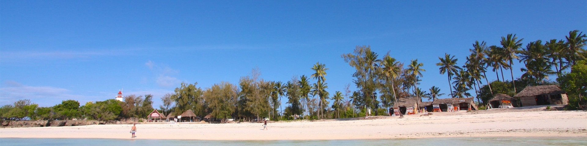 Uma praia com águas turquesa cristalinas, palmeiras e cabanas com telhado de palha.