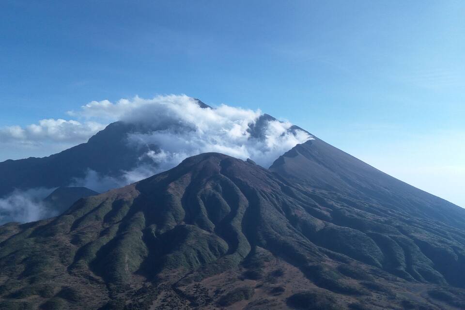 A mountain with a prominent peak, lush green vegetation, and clouds at the summit.