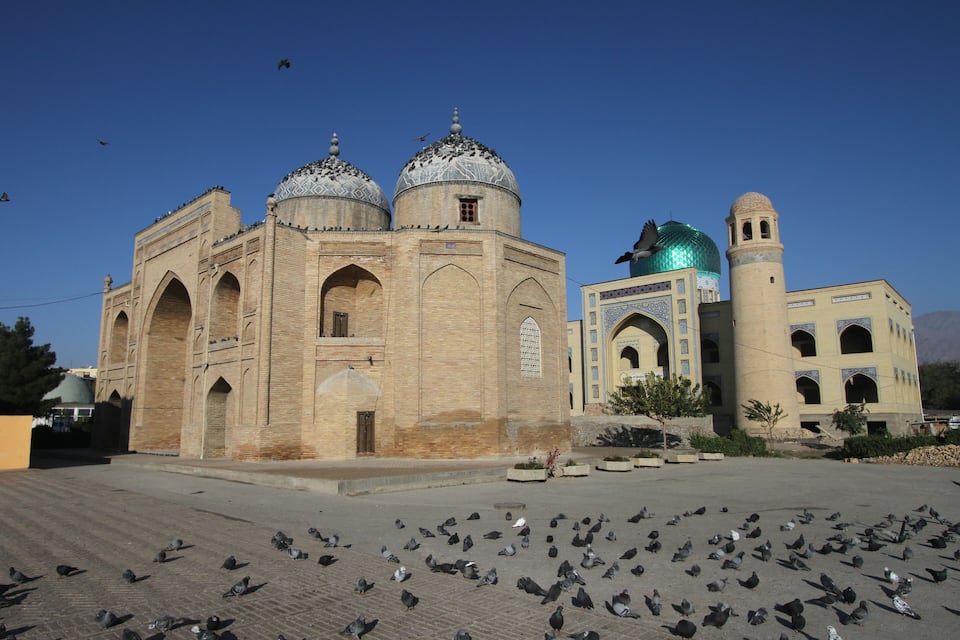Um edifício histórico com cúpulas e um minarete, rodeado por pombos.