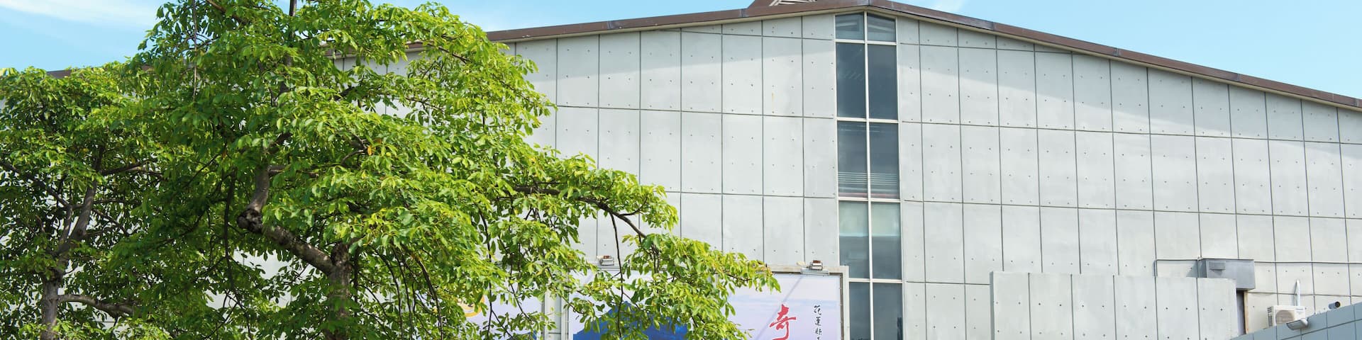 Un edificio moderno con carteles grandes y un árbol en primer plano.