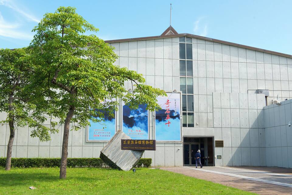 A modern building with large posters and a tree in front.