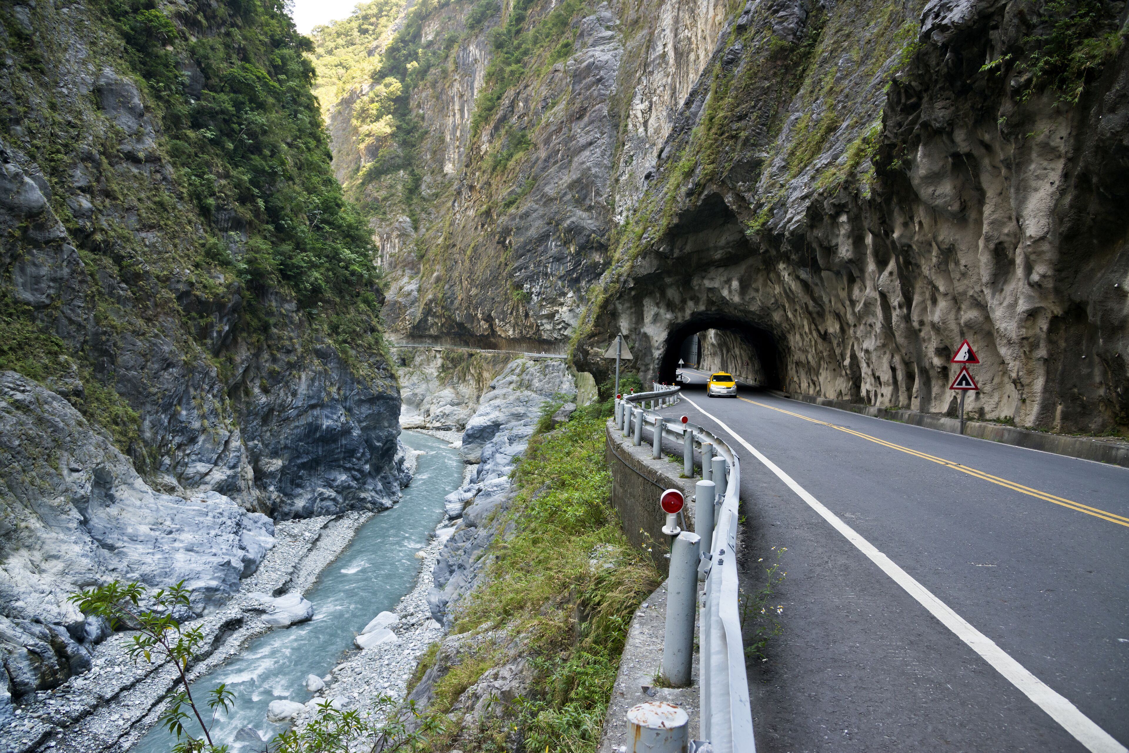 En vej der løber gennem en klippefyldt kløft med en flod på den ene side og en tunneltilgang på den anden.
