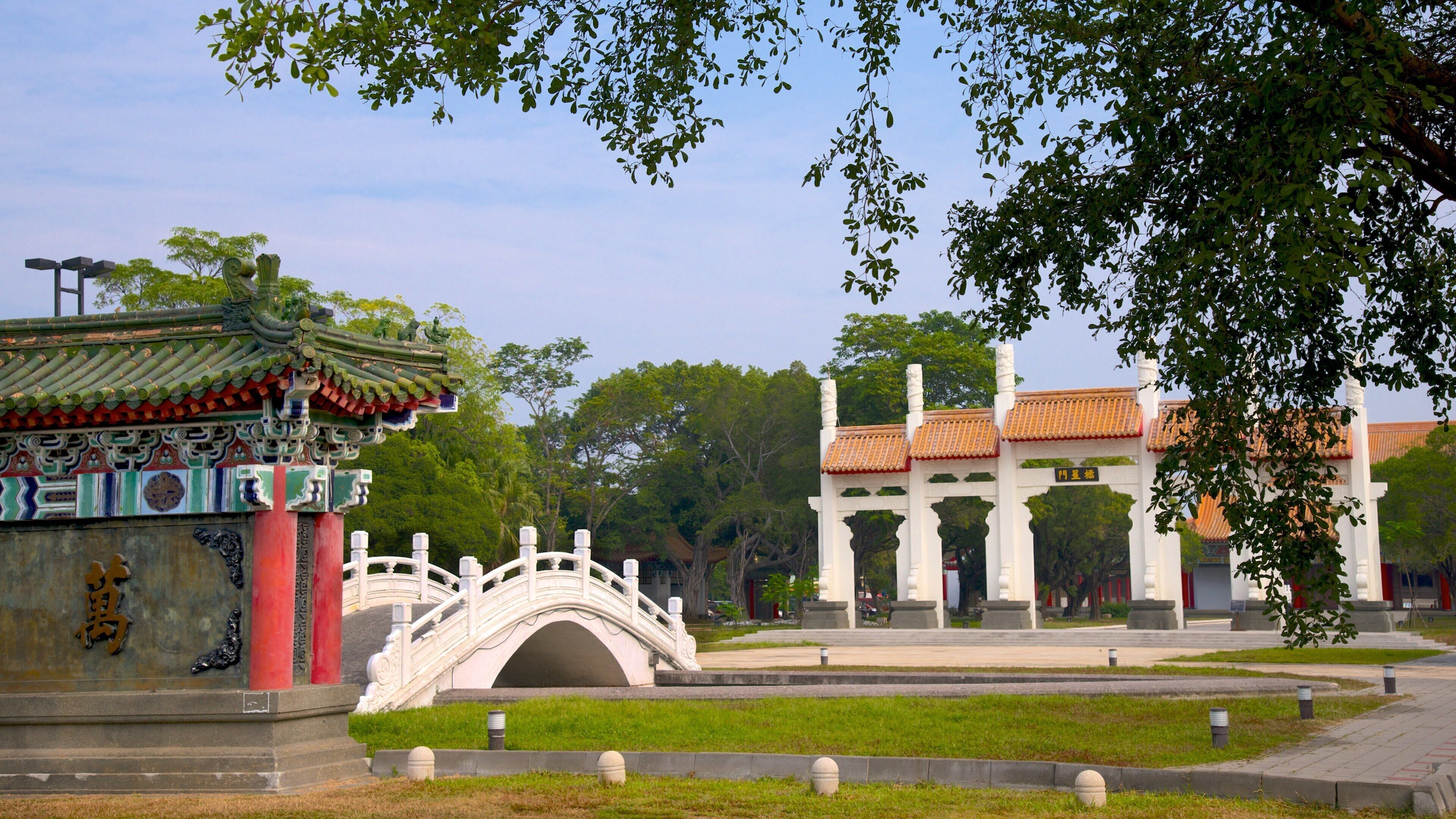 A traditional Chinese pavilion with a tiled roof, a stone bridge, and a white building with columns.
