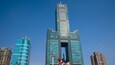 A tall skyscraper with a distinctive top and a central void, surrounded by other high-rise buildings.
