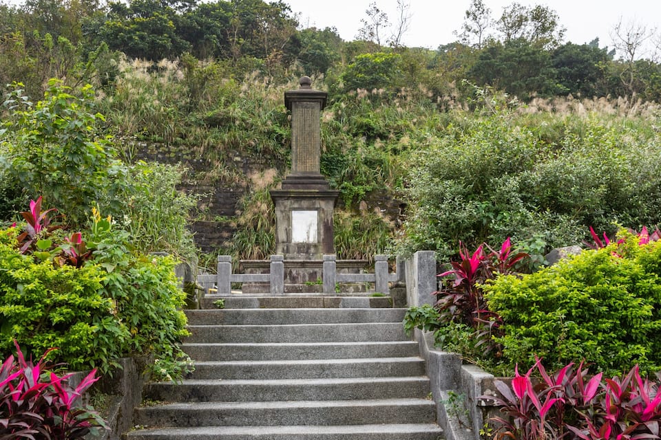 A stone staircase leading up to a stone monument surrounded by lush greenery and flowering plants.