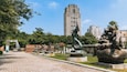 Un parque con esculturas, un camino pavimentado y edificios altos al fondo.