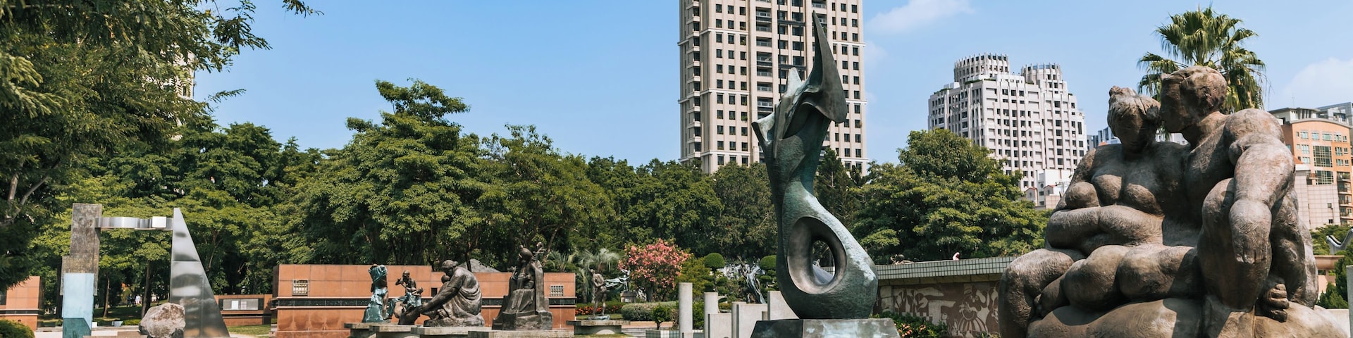 Ein Park mit Skulpturen, einem gepflasterten Weg und hohen Gebäuden im Hintergrund.