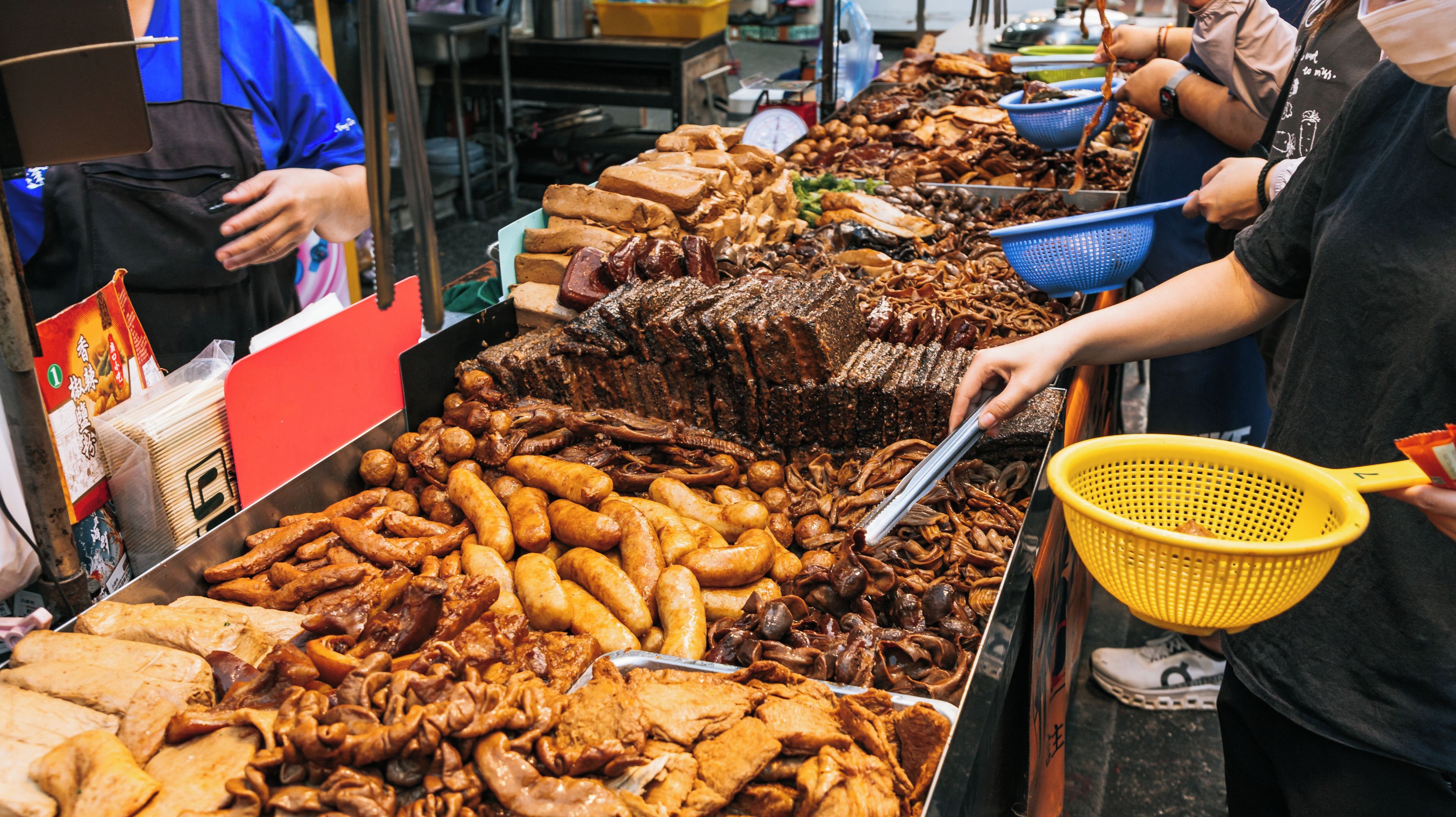 A variety of fried foods, including sausages, meat, and possibly seafood, displayed at a market stall.
