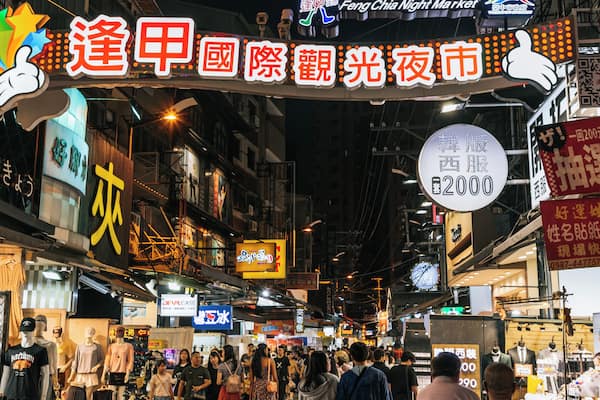 A bustling street market with illuminated signs and mannequins displaying clothing.