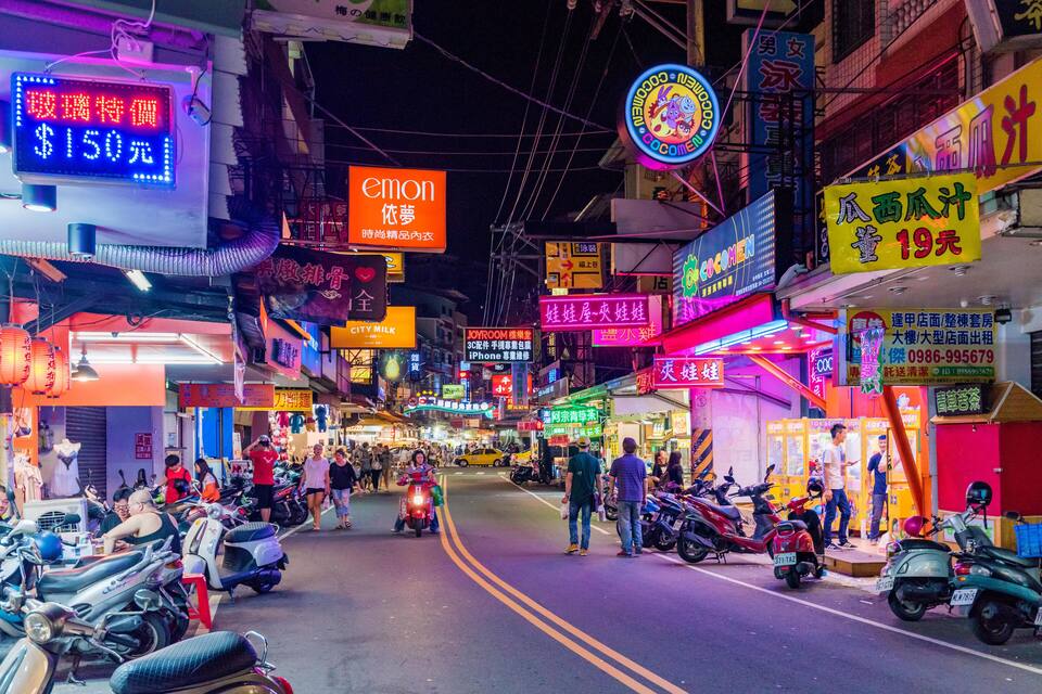 Una calle concurrida por la noche, con letreros de neón y scooters.