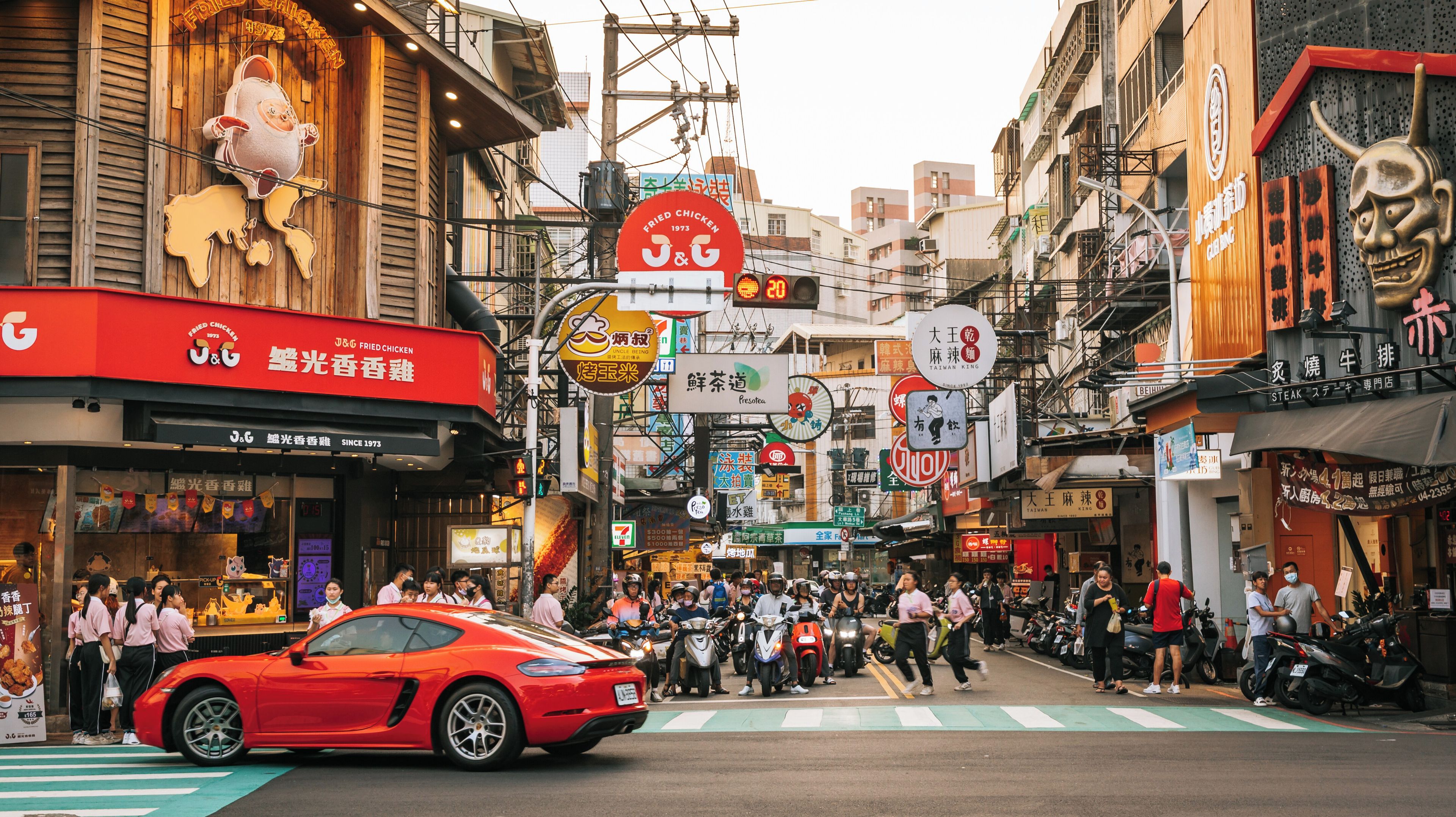 A busy street with various shops, motorcycles, and a red sports car.
