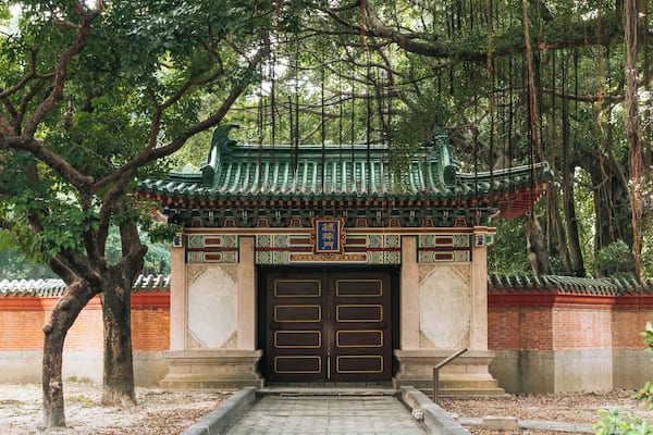 Ein traditionelles chinesisches Tor mit aufwendiger Dekoration und einem Ziegeldach, umgeben von Bäumen.
